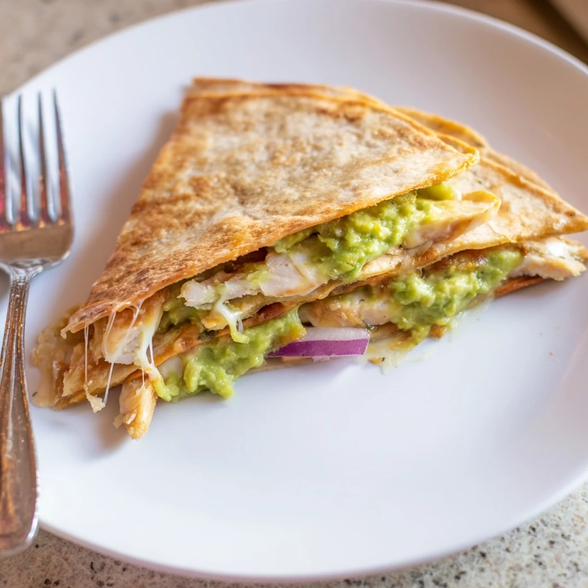 A close-up of a warm Chicken Avocado Quesadilla slice revealing gooey Monterey Jack, sliced chicken, and red onion on a rustic plate.