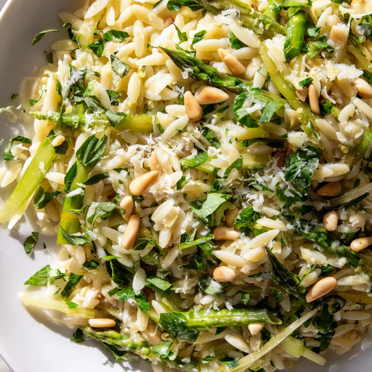 ASPARAGUS LEMON ORZO SALAD mit knusprigen Pinienkernen, frischer Petersilie und glänzendem Zitronen-Dressing angerichtet.