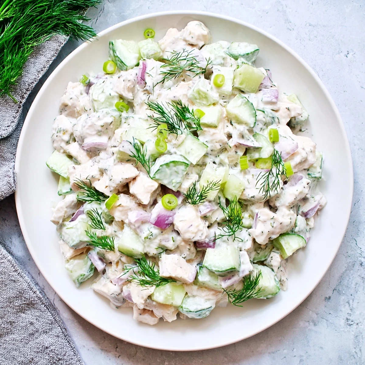 Cremige Gurken Hühnchensalat auf einem hellen Teller, mit knusprigen Gurkenscheiben und frischem Dill garniert.