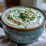 A bowl of Creamy Celery Root Bisque drizzled with cream, paired with crusty bread on a linen tablecloth for a cozy dinner.