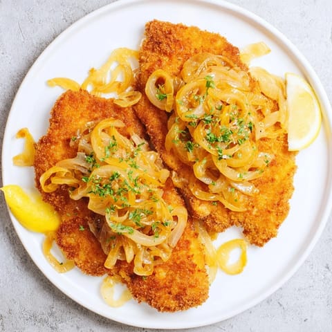 A close-up of a tender Schnitzel with caramelized onions, ready to be enjoyed with lemon wedges.