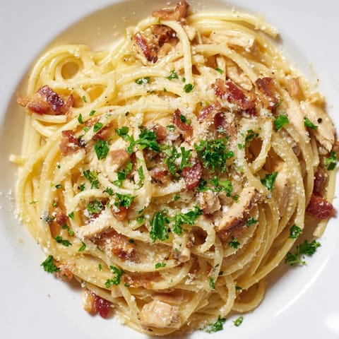 Ein Teller nudeliger Carbonara mit Hähnchenfleisch und knusprigem Bacon liegt neben einem Glas Weißwein.